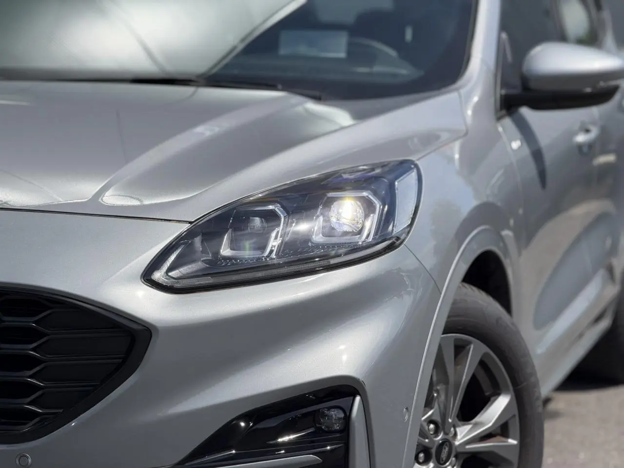 Vue 3/4 avant droit du Ford Kuga gris Solar mettant en valeur le phare Full LED et la calandre noire hexagonale.