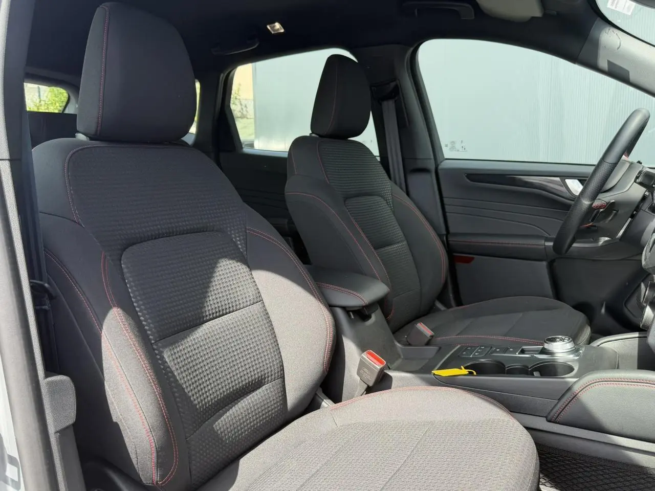 Vue intérieure côté gauche montrant les sièges avant noirs avec surpiqûres rouges du Ford Kuga ST-Line 2023.