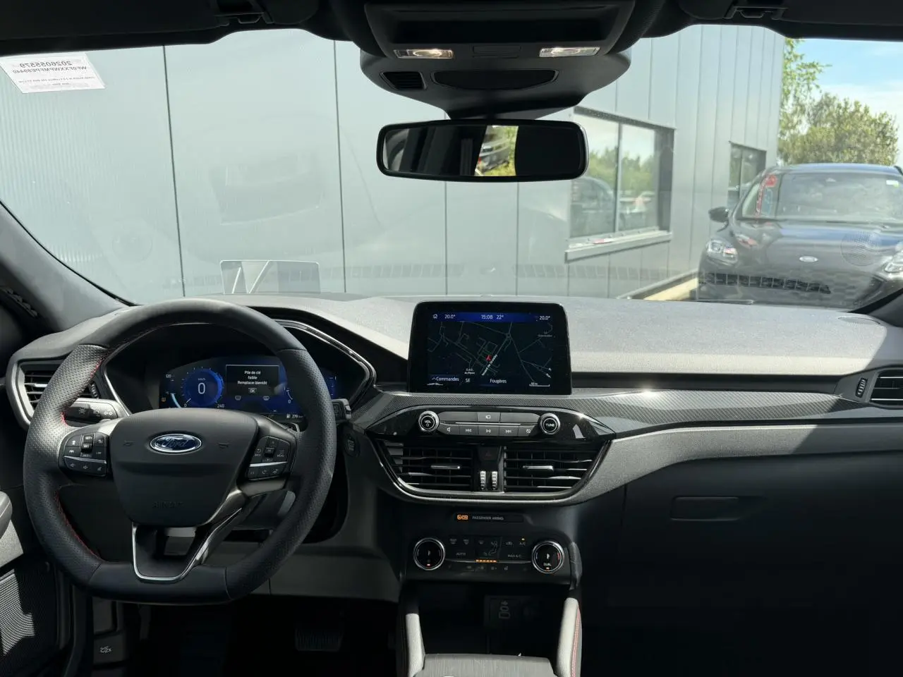 Vue intérieure avant du Ford Kuga 2023 ST-Line, tableau de bord noir avec écran tactile central et volant multifonction à surpiqûres rouges.