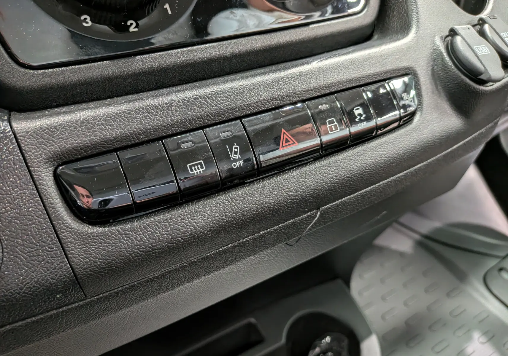 Gros plan sur la rangée de boutons noirs du tableau de bord du Fiat Ducato Fourgon blanc, avec commandes de sécurité et verrouillage.