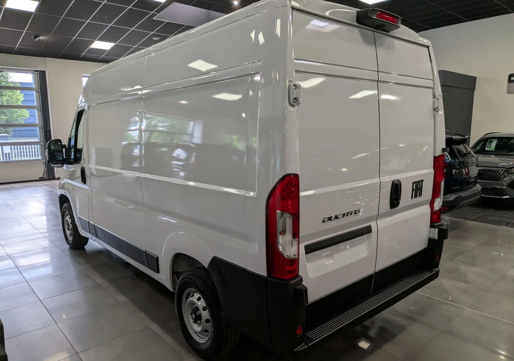 Vue 3/4 arrière droite d’un FIAT Ducato Fourgon blanc, avec portes arrière fermées et pare-chocs noir dans un showroom.
