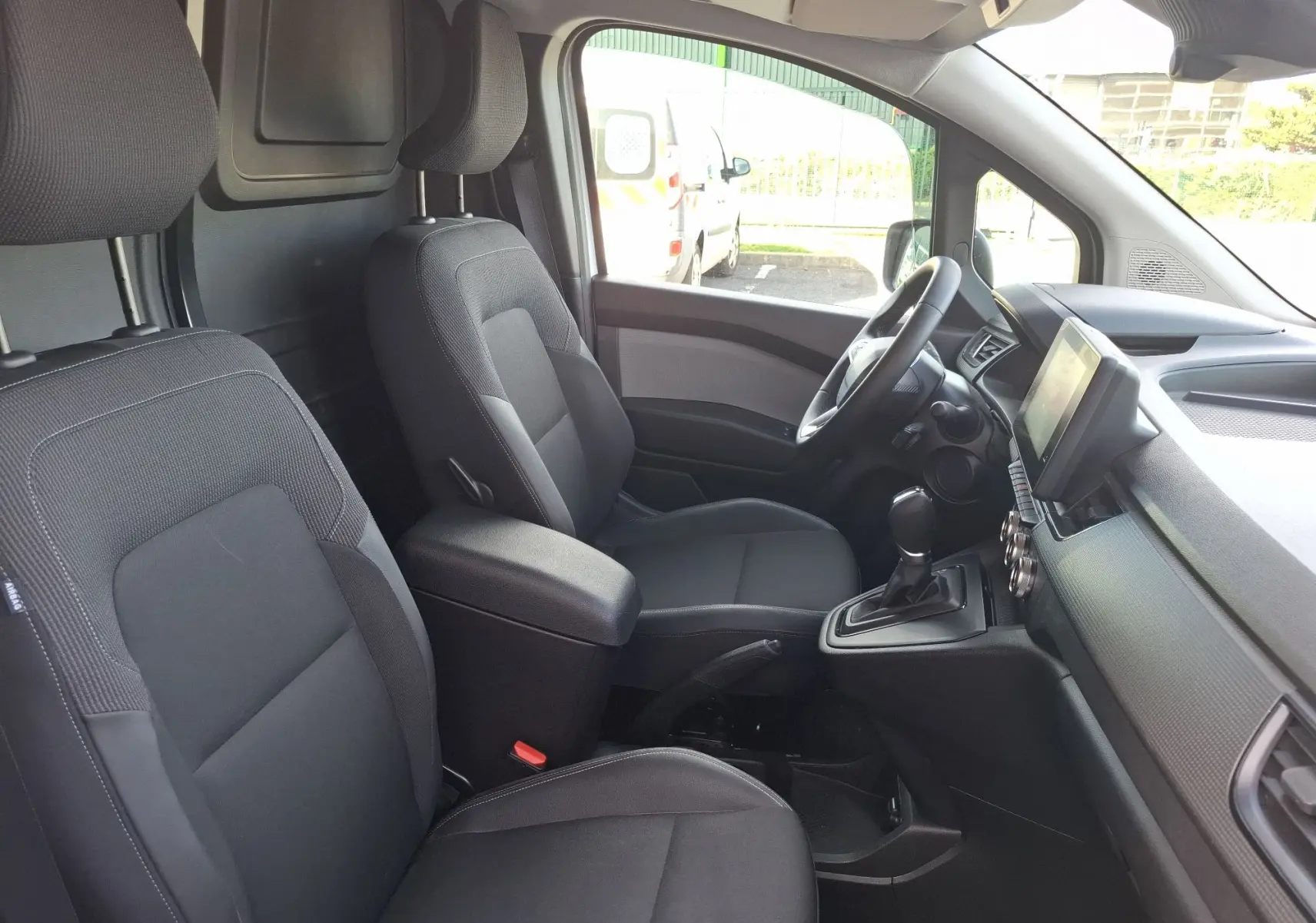 Vue intérieure côté conducteur du Renault Kangoo Pro blanc 2025, montrant sièges noirs et tableau de bord moderne.