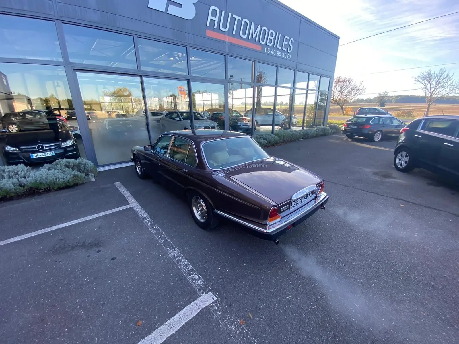 Jaguar XJ6 Série 3 4.2 Sovereign marron vue 3/4 arrière droit sur parking devant un showroom automobile.