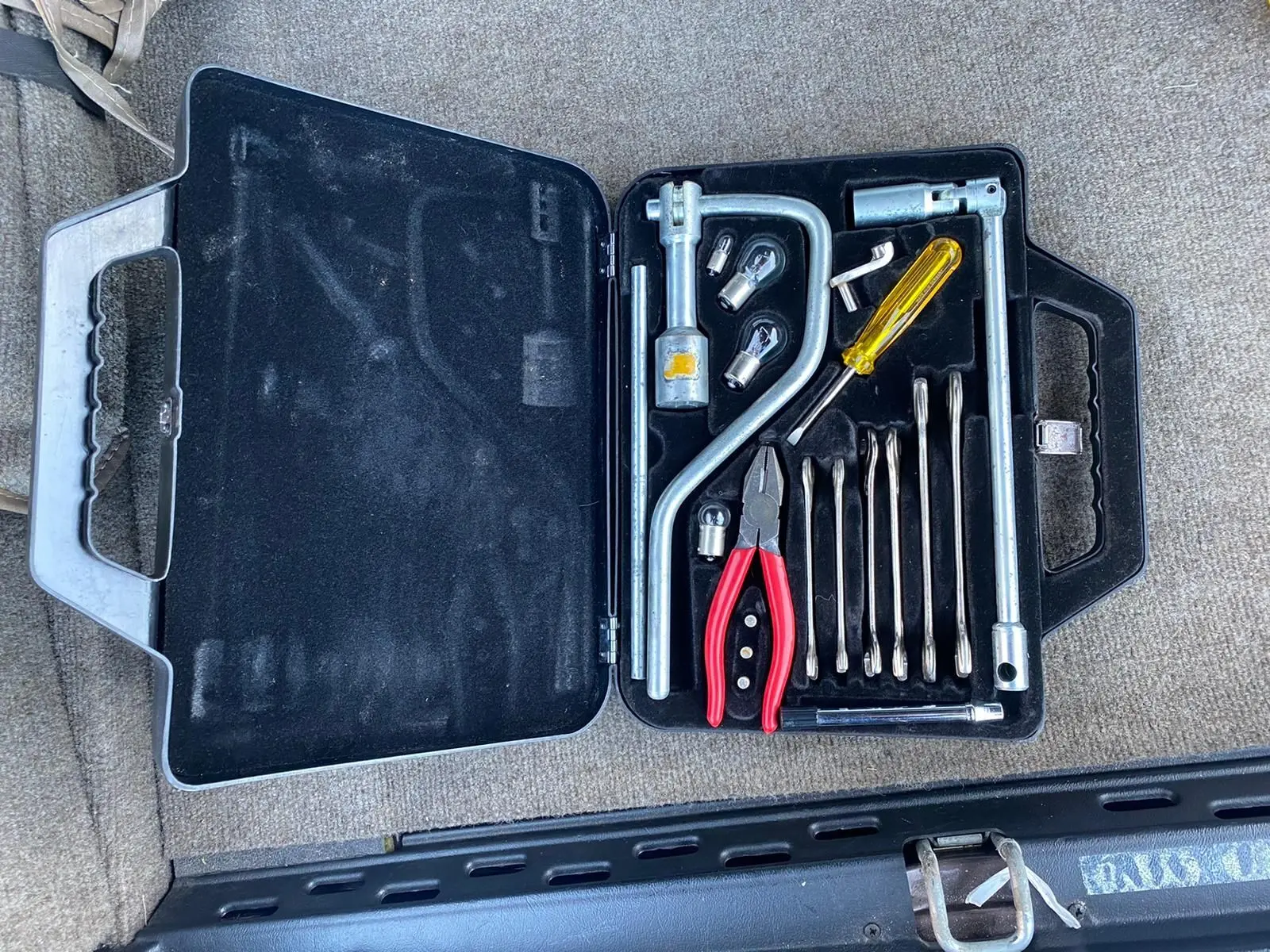 Boîte à outils ouverte avec pinces rouges et tournevis jaune, posée sur la moquette marron d'une Jaguar XJ6 Série 3 1985.