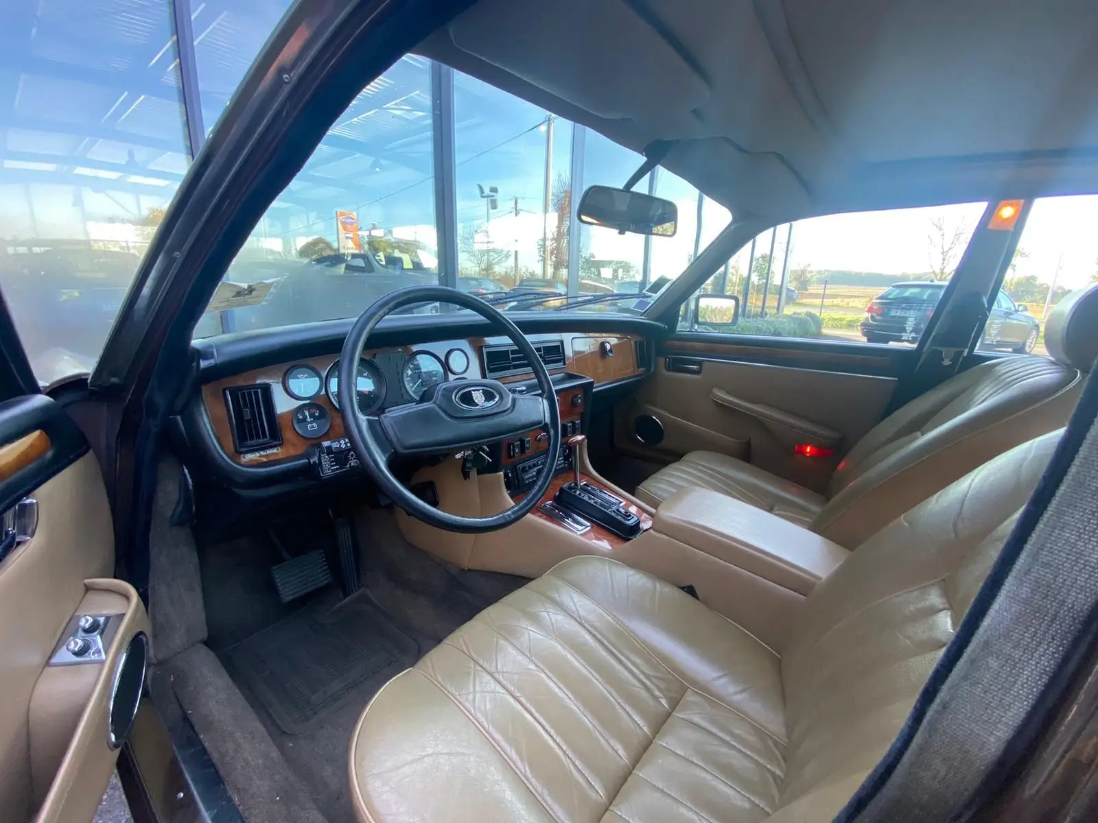 Intérieur beige du Jaguar XJ6 Série 3 4.2 Sovereign 1985, vue côté conducteur avec tableau de bord en bois et volant noir.