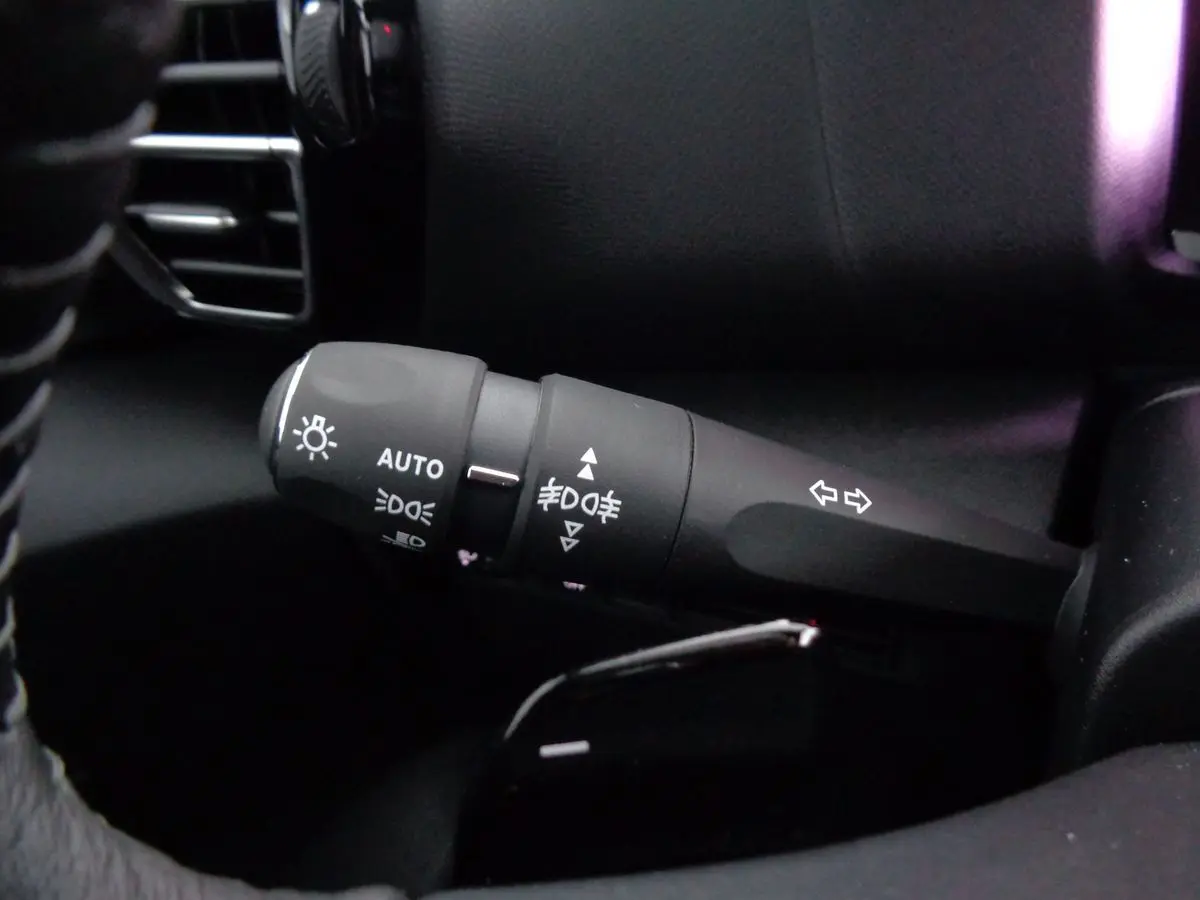 Gros plan sur la commande des phares et clignotants à gauche du volant dans l’habitacle noir du Citroën C4 gris 2023.
