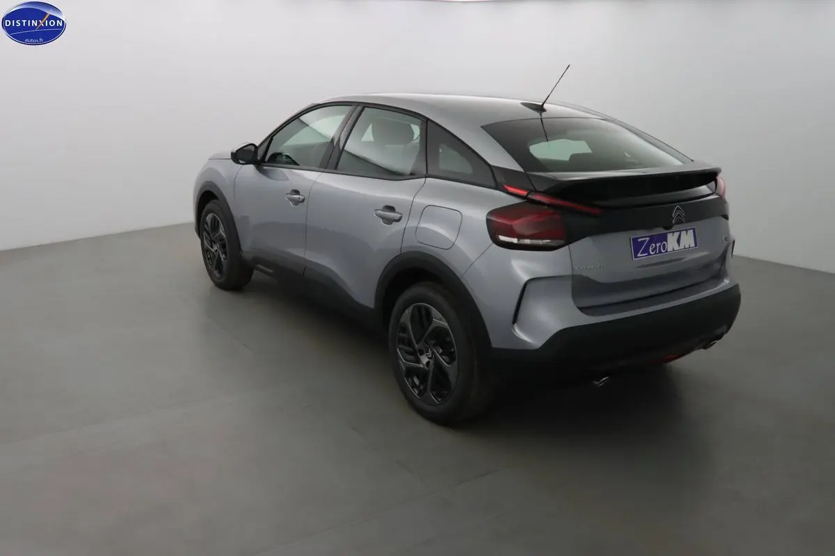 Vue 3/4 arrière droite d'une Citroën C4 2023 gris Artense métallisé avec toit noir et jantes bi-ton.