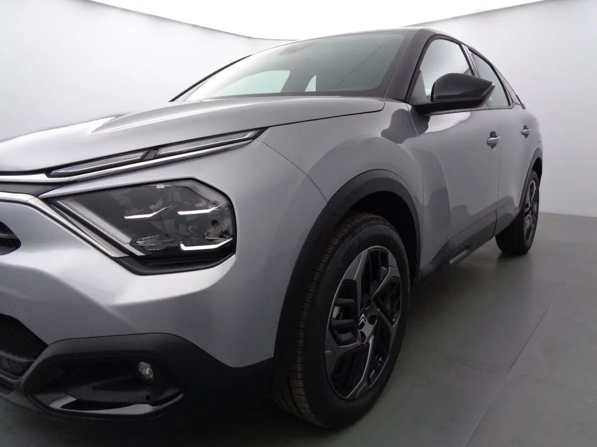 Vue 3/4 avant droit d'une Citroën C4 2023 gris Artense métal avec phares modernes et jantes noires bicolores.