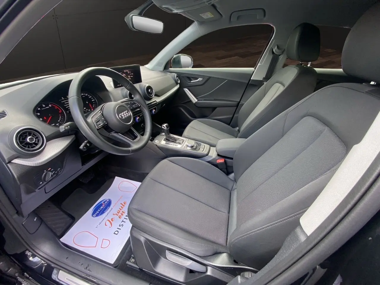 Intérieur avant de l'Audi Q2 35 TFSI 2023 en tissu noir, vue côté conducteur avec tableau de bord et volant visibles.