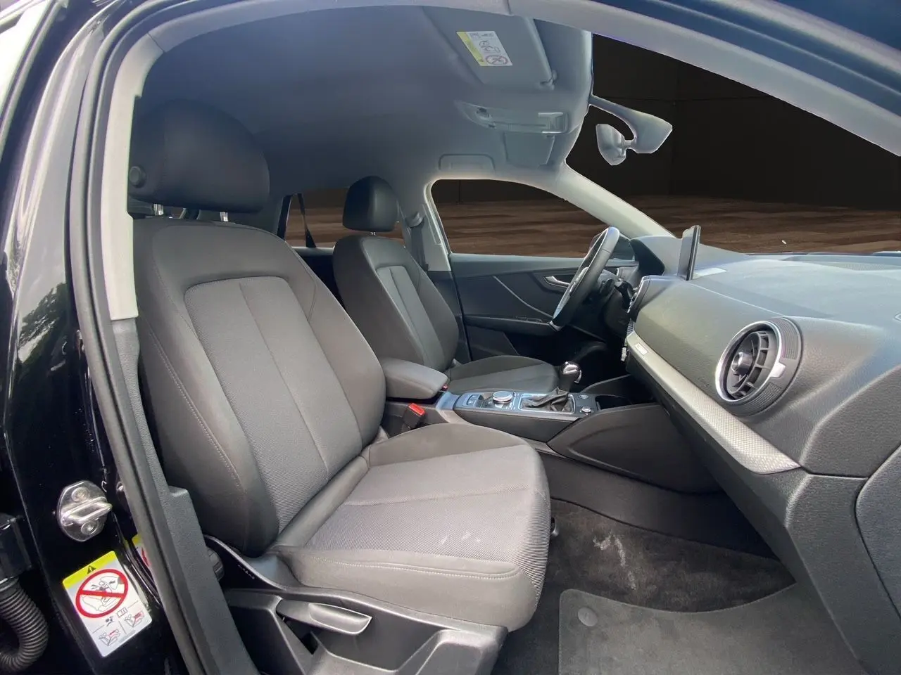 Intérieur avant droit de l'Audi Q2 noir mito 2023, sièges tissu noir et tableau de bord moderne avec écran GPS.