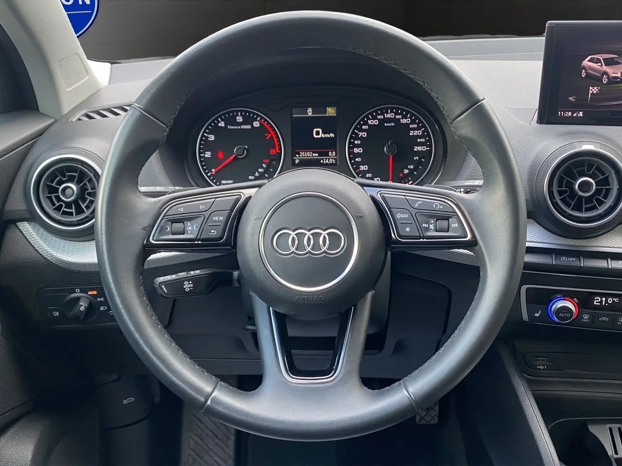 Vue intérieure centrée sur le volant cuir noir de l'Audi Q2 35 TFSI avec tableau de bord et écran GPS visible.