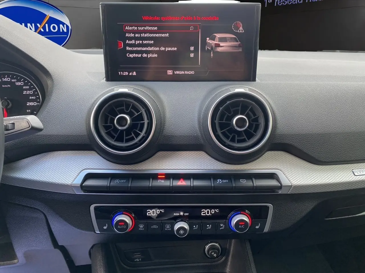 Tableau de bord intérieur d'Audi Q2 2023 avec écran central affichant aides à la conduite et commandes climatisation.