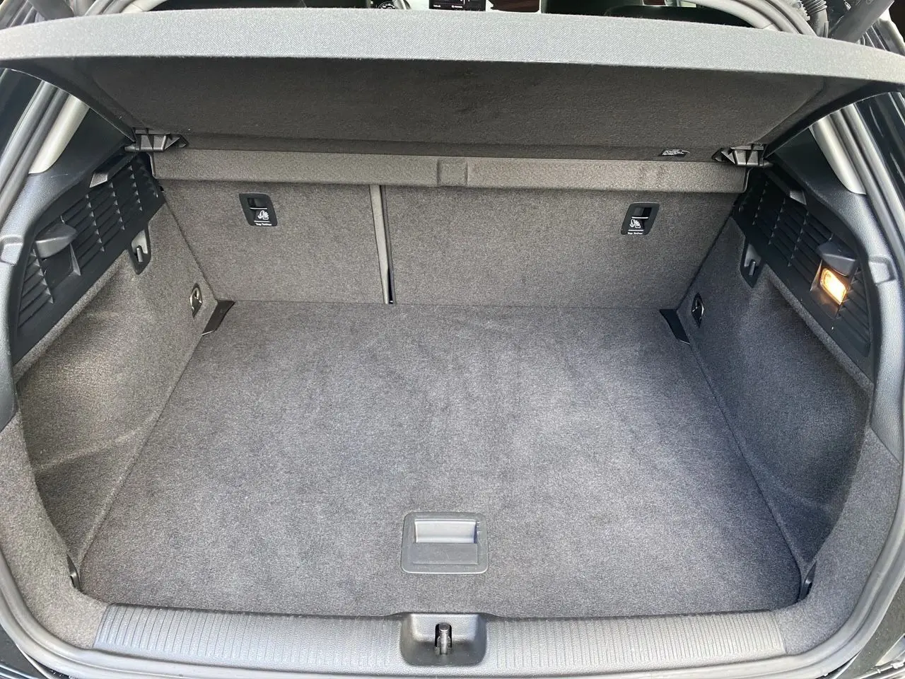 Coffre spacieux ouvert d’un Audi Q2 noir Mito, montrant la moquette grise et les fixations Isofix arrière.