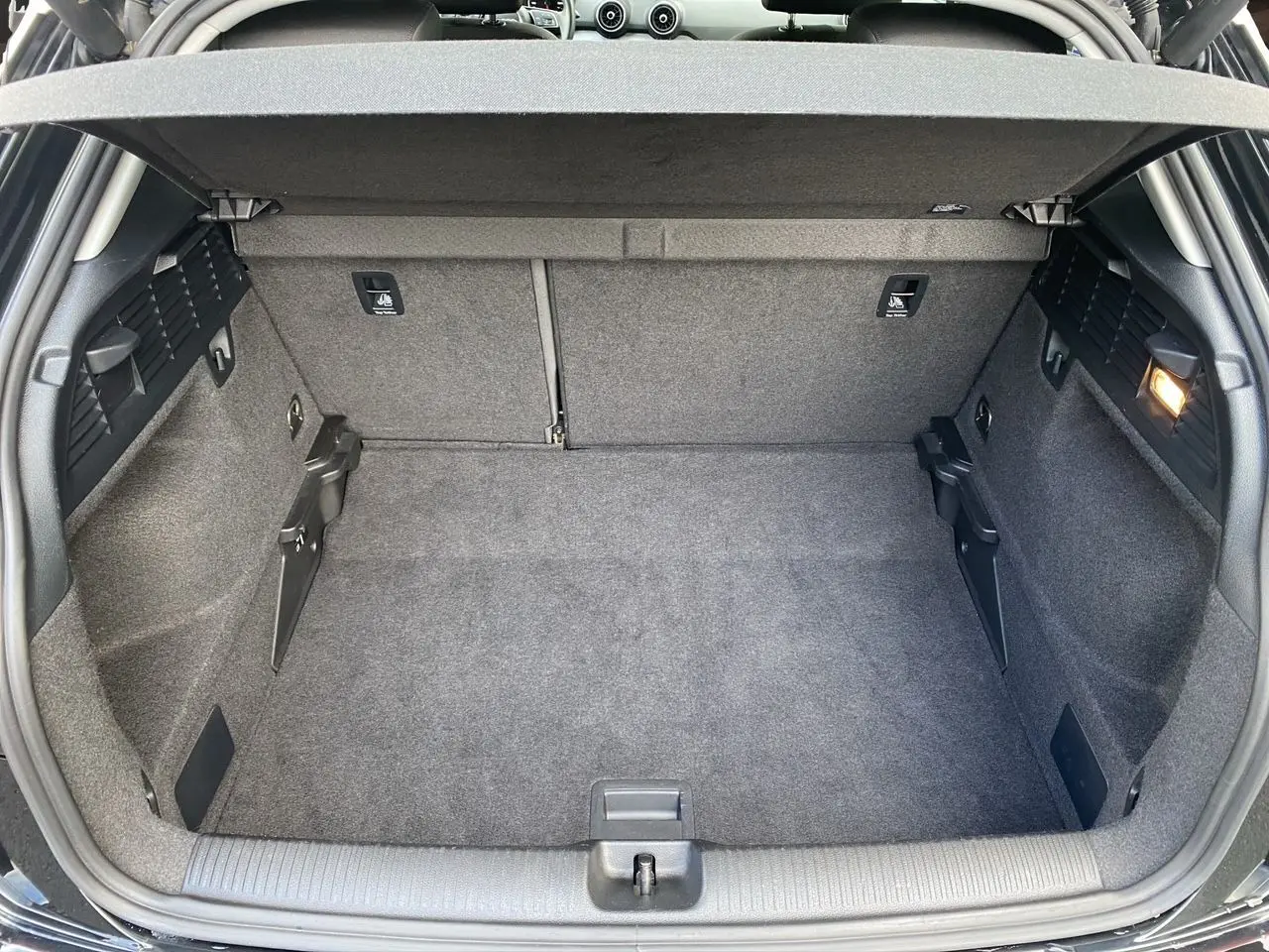 Détail du tableau de bord noir de l'Audi Q2 35 TFSI 2023 montrant la commande des phares et le levier de régulateur de vitesse.