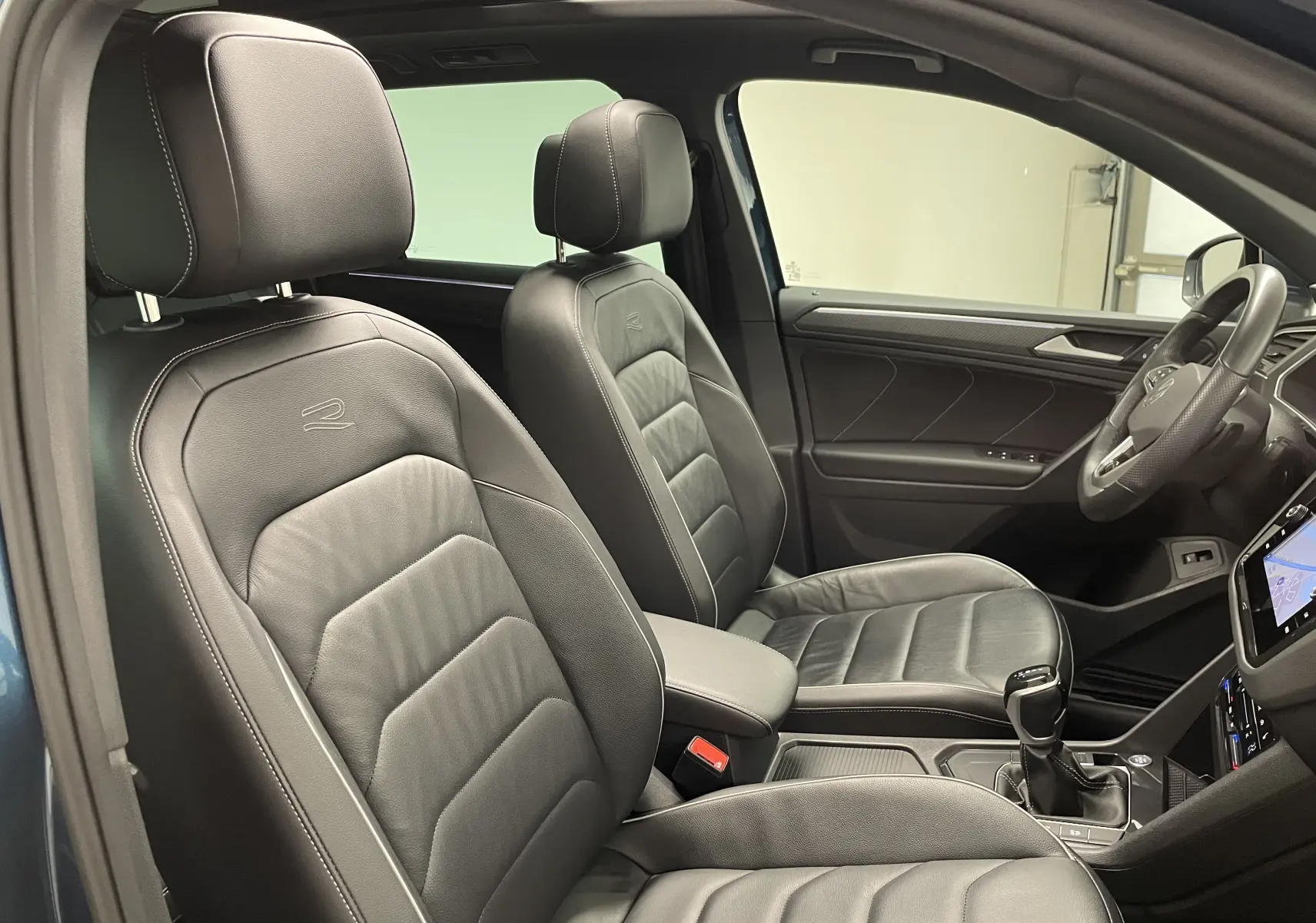 Intérieur du Volkswagen Tiguan 2024 en vue latérale côté conducteur, sièges cuir noirs avec logo R brodé.