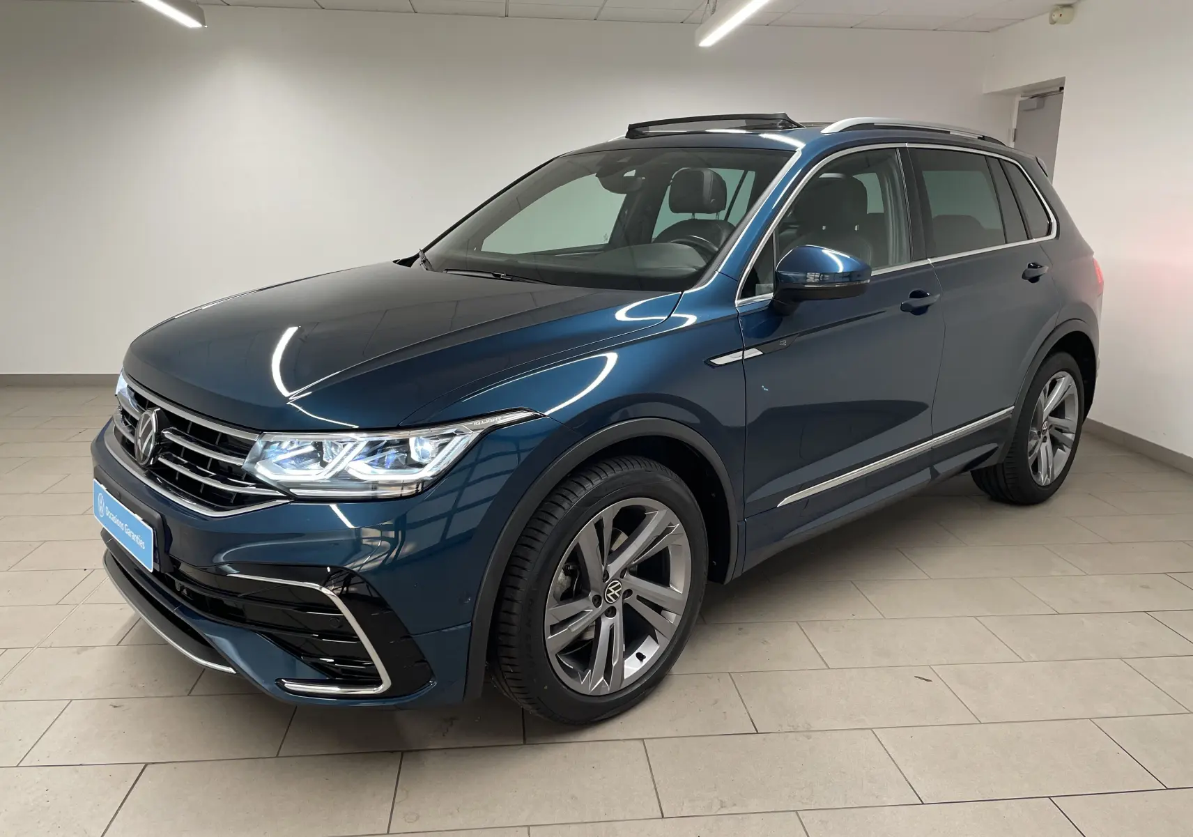 Volkswagen Tiguan 2024 bleu Nightshade en vue 3/4 avant droit, avec jantes alliage et attelage escamotable visible.
