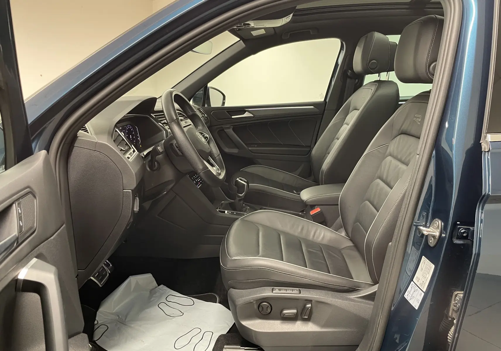 Vue intérieure côté conducteur du Volkswagen Tiguan 2024 en Nightshade Blue avec sièges cuir R-Line et tableau de bord moderne.