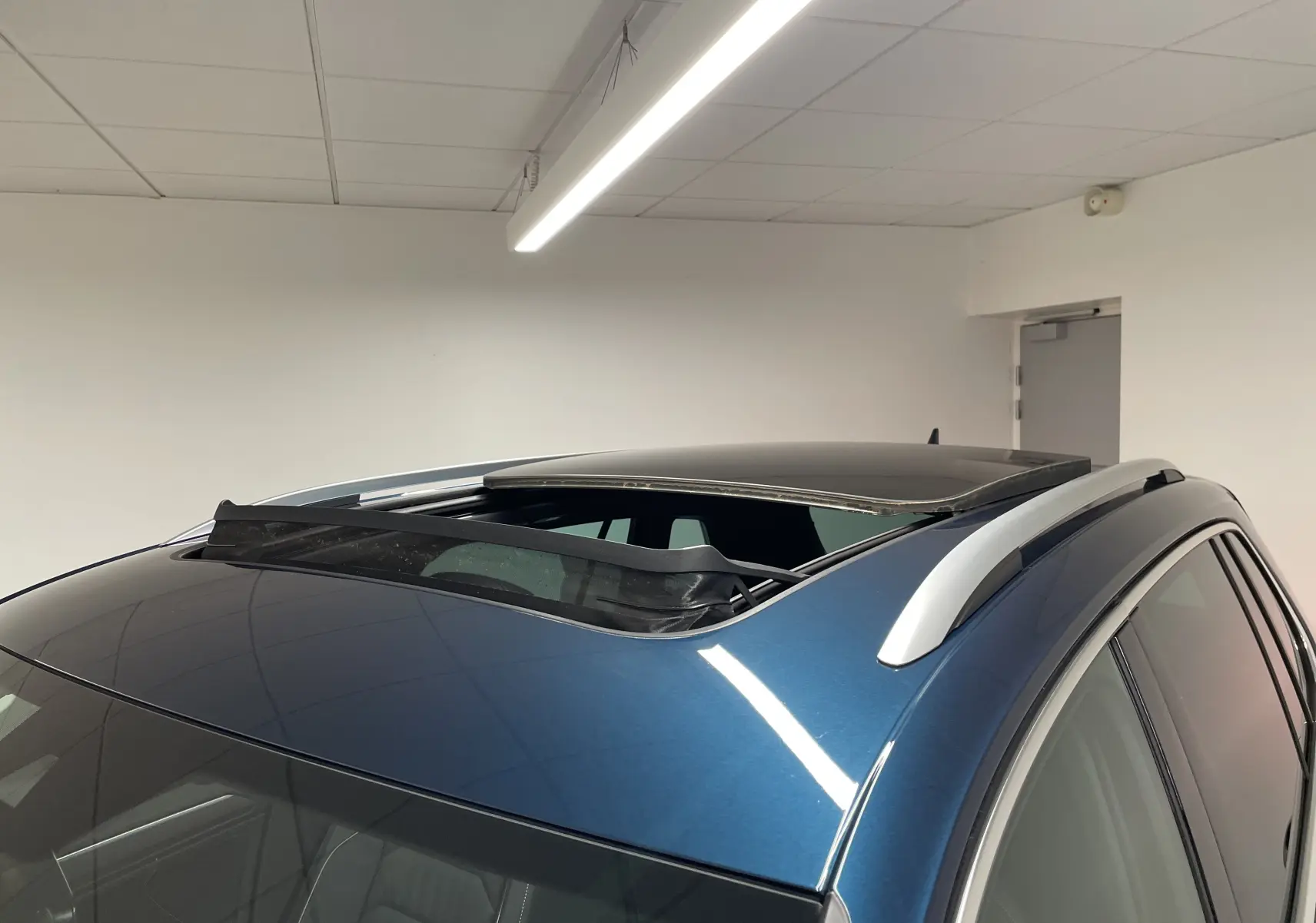 Toit ouvrant panoramique ouvert sur le dessus d'un Volkswagen Tiguan 2024 bleu Nightshade avec barres de toit argentées.