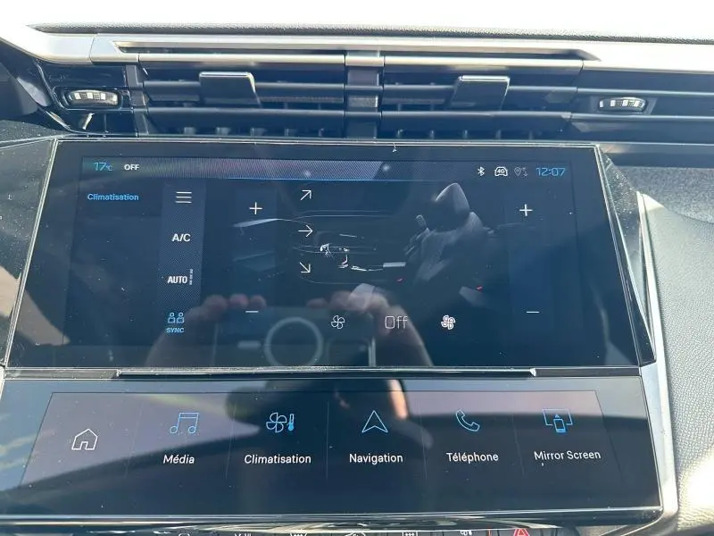Écran tactile central de la Peugeot 308 bleu, vue rapprochée du système multimédia et climatisation.