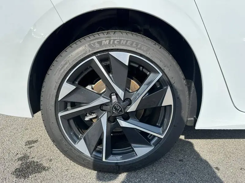 Gros plan sur la roue arrière droite d'une Peugeot 308 blanche, jante alu noire et grise au design géométrique.