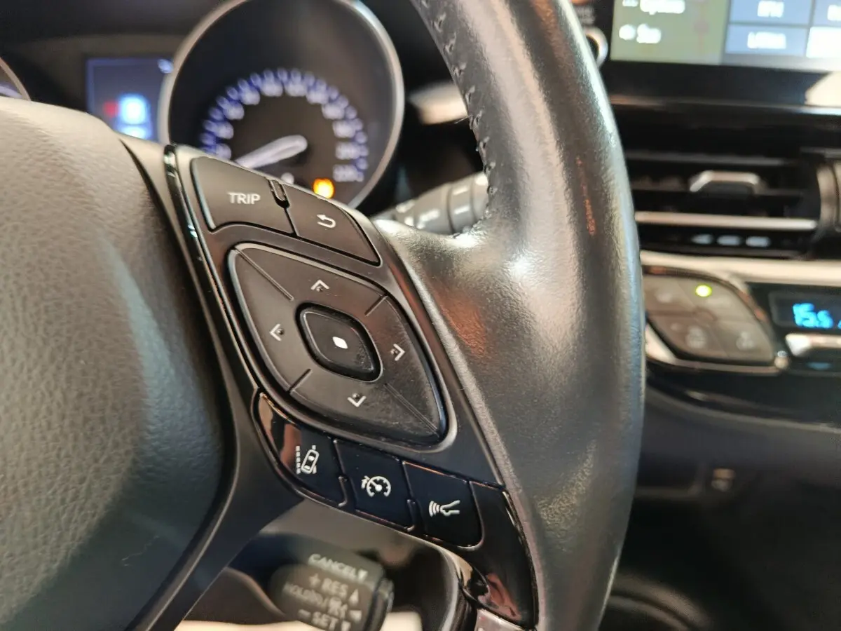 Gros plan sur le volant cuir du Toyota C-HR gris clair 2022, avec commandes multifonctions et tableau de bord en arrière-plan.