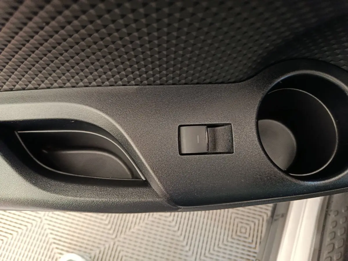 Gros plan sur la poignée de porte intérieure noire et le bouton de verrouillage d’un Toyota C-HR gris clair.