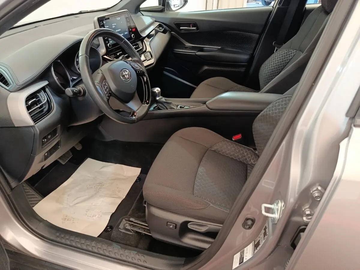 Intérieur côté conducteur du Toyota C-HR gris clair 2022, avec tableau de bord moderne et sièges tissu noirs.