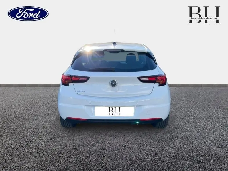 Vue arrière d'une Opel Astra blanche Glacier de 2020, avec feux arrière sombres et logo central visible.