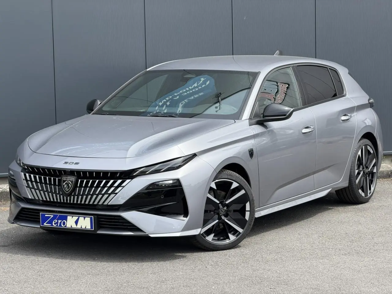 Peugeot 308 gris Artense vue 3/4 avant, avec calandre noire distinctive et jantes alliage bi-ton.
