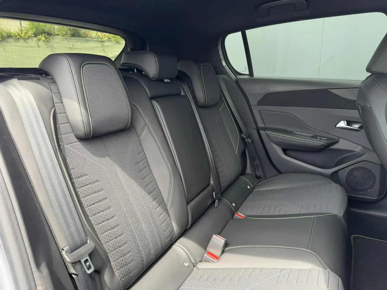 Vue latérale intérieure des sièges arrière en tissu noir avec surpiqûres vertes de la Peugeot 308 NV Hybrid 145 GT e-DSC6.