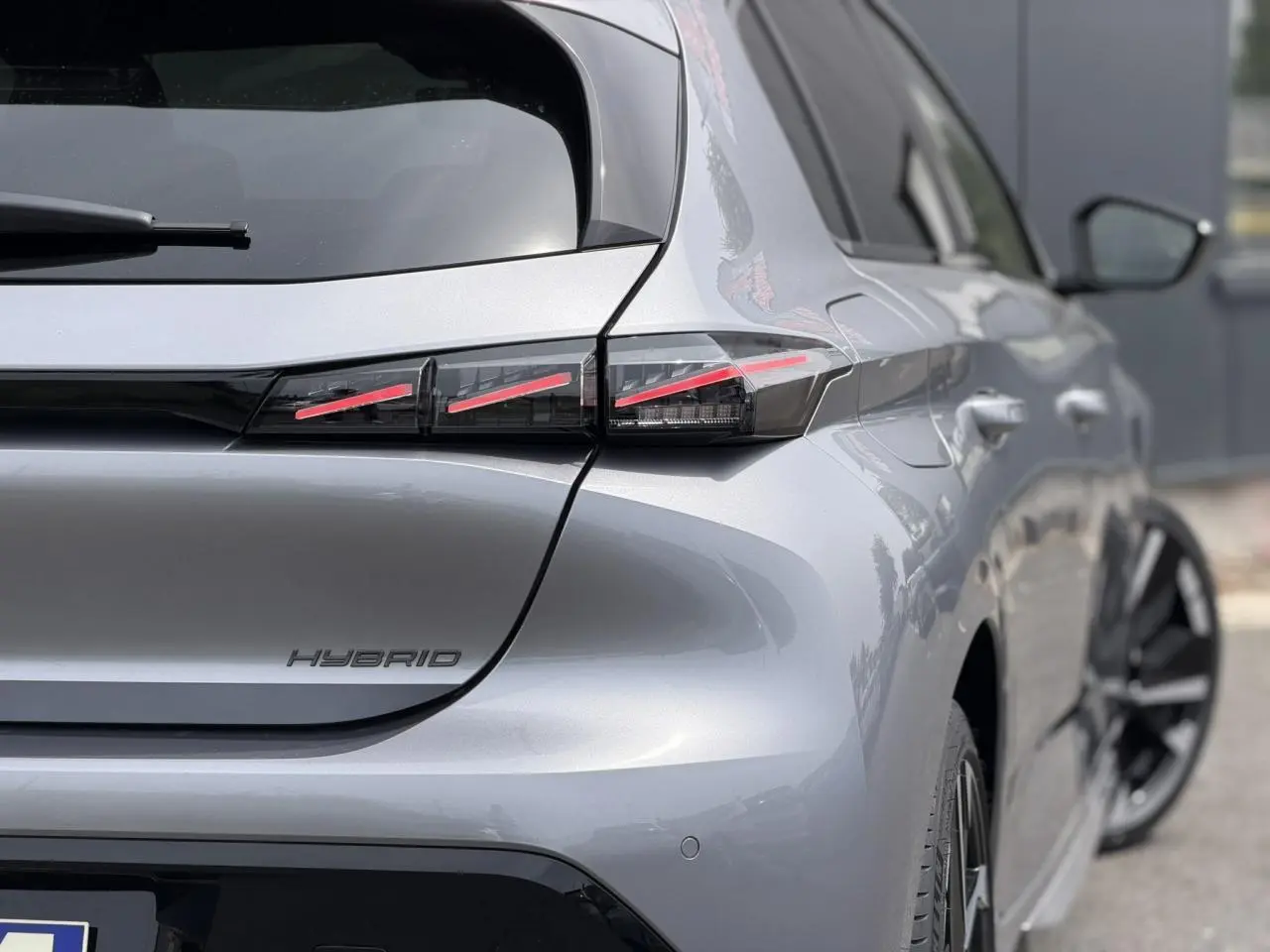 Vue 3/4 arrière droite d'une Peugeot 308 Hybrid gris Artense avec feux arrière LED à 3 griffes et jantes bi-tons.