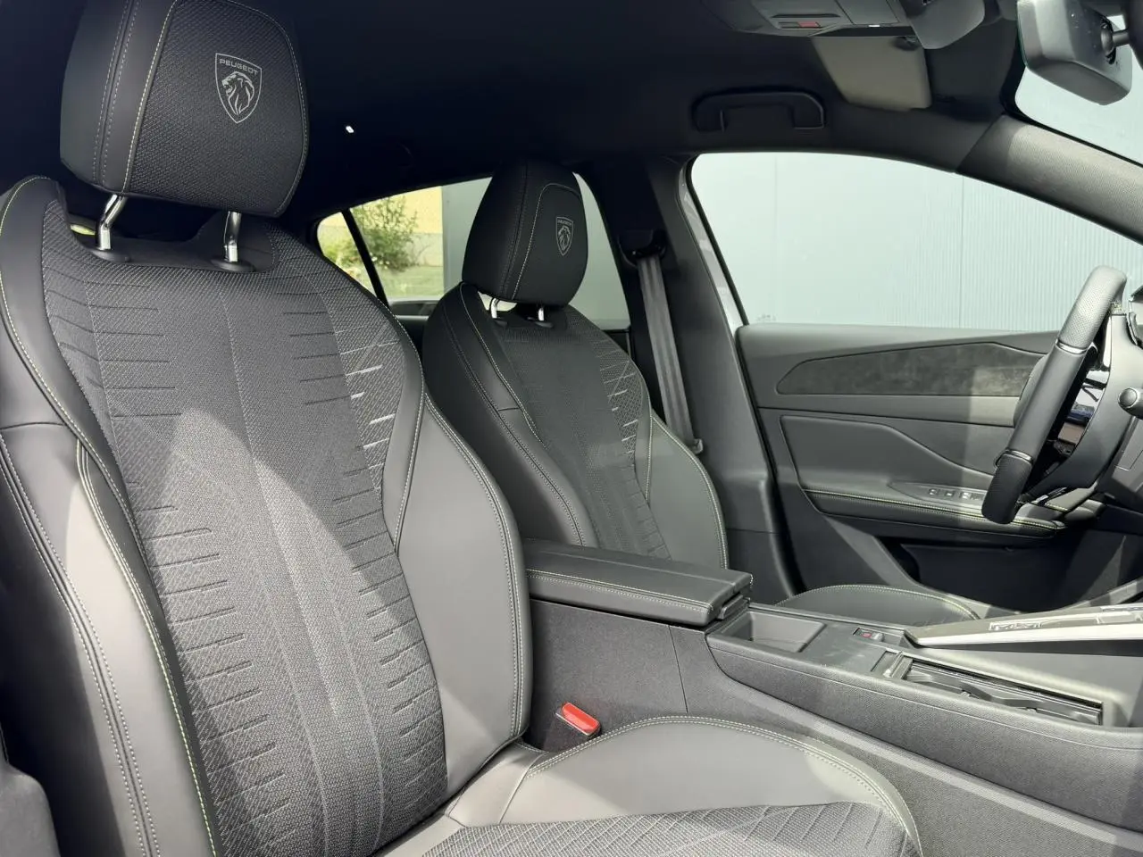 Vue intérieure côté gauche des sièges avant noirs avec surpiqûres vert Adamite et blasons Peugeot embossés sur appuie-têtes.