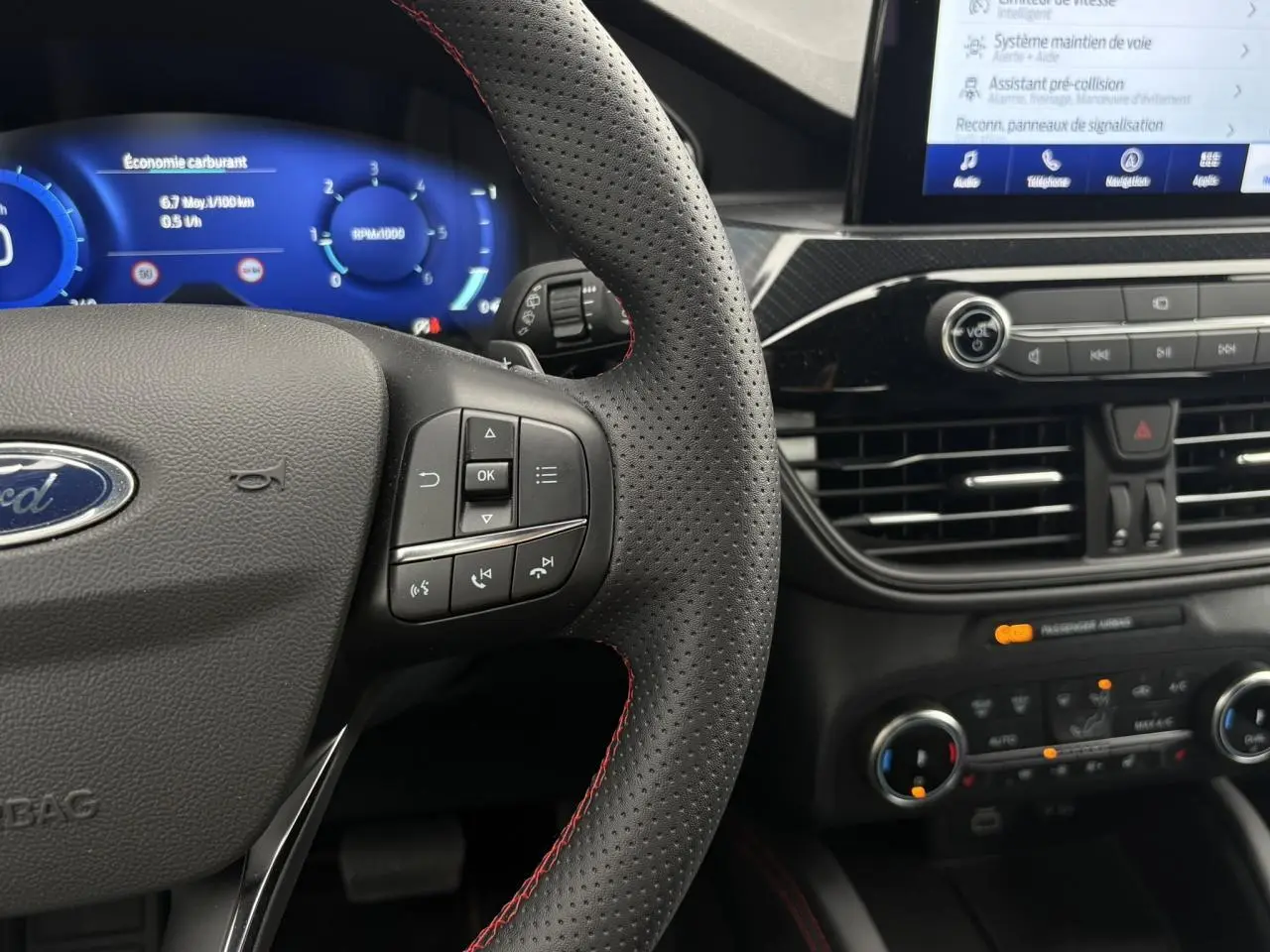 Vue rapprochée du volant perforé noir avec surpiqûres rouges et tableau de bord numérique du Ford Kuga 2023.