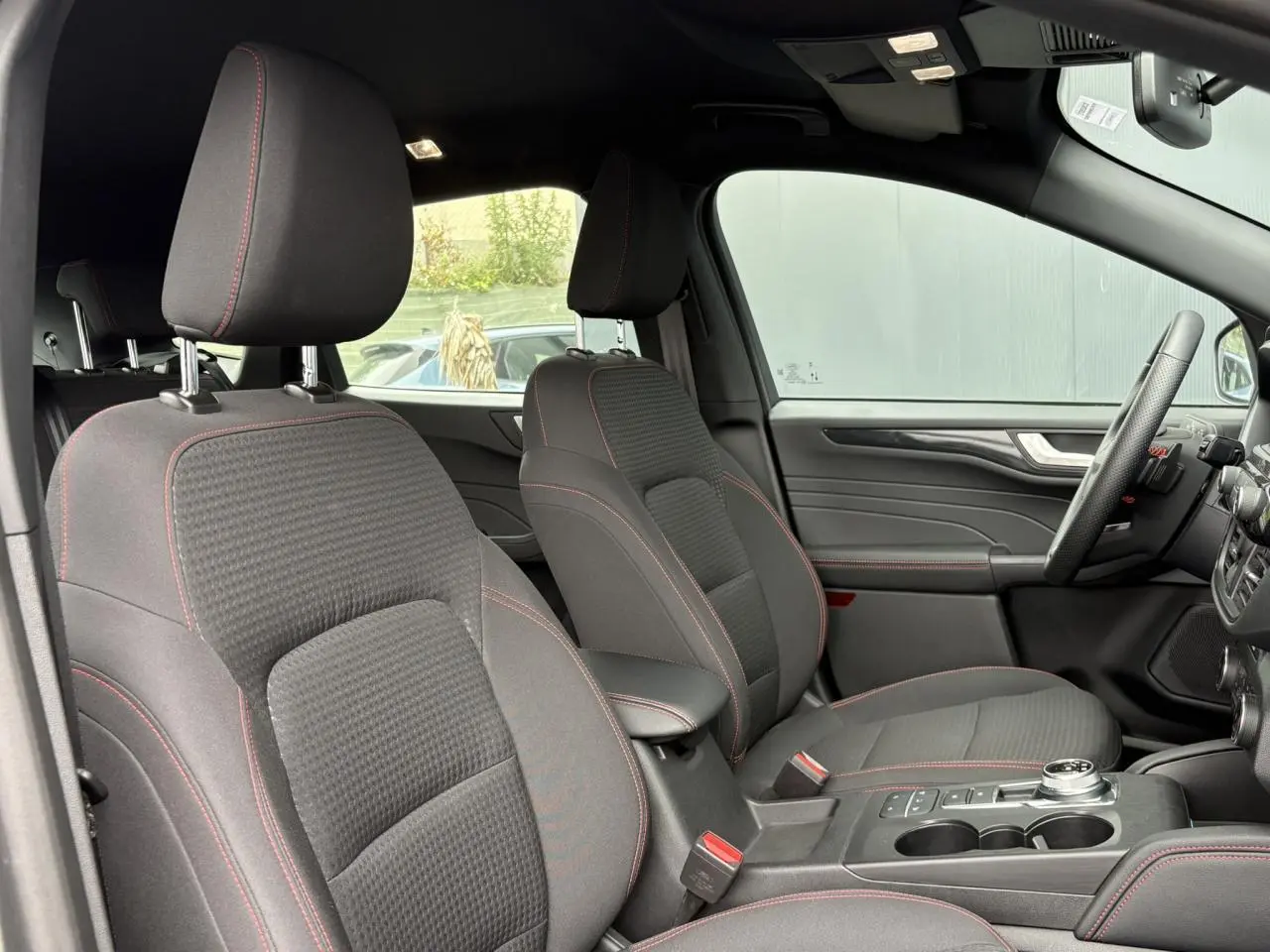 Vue intérieure côté conducteur du Ford Kuga 2023, sièges gris avec surpiqûres rouges et volant ST-Line à méplat.
