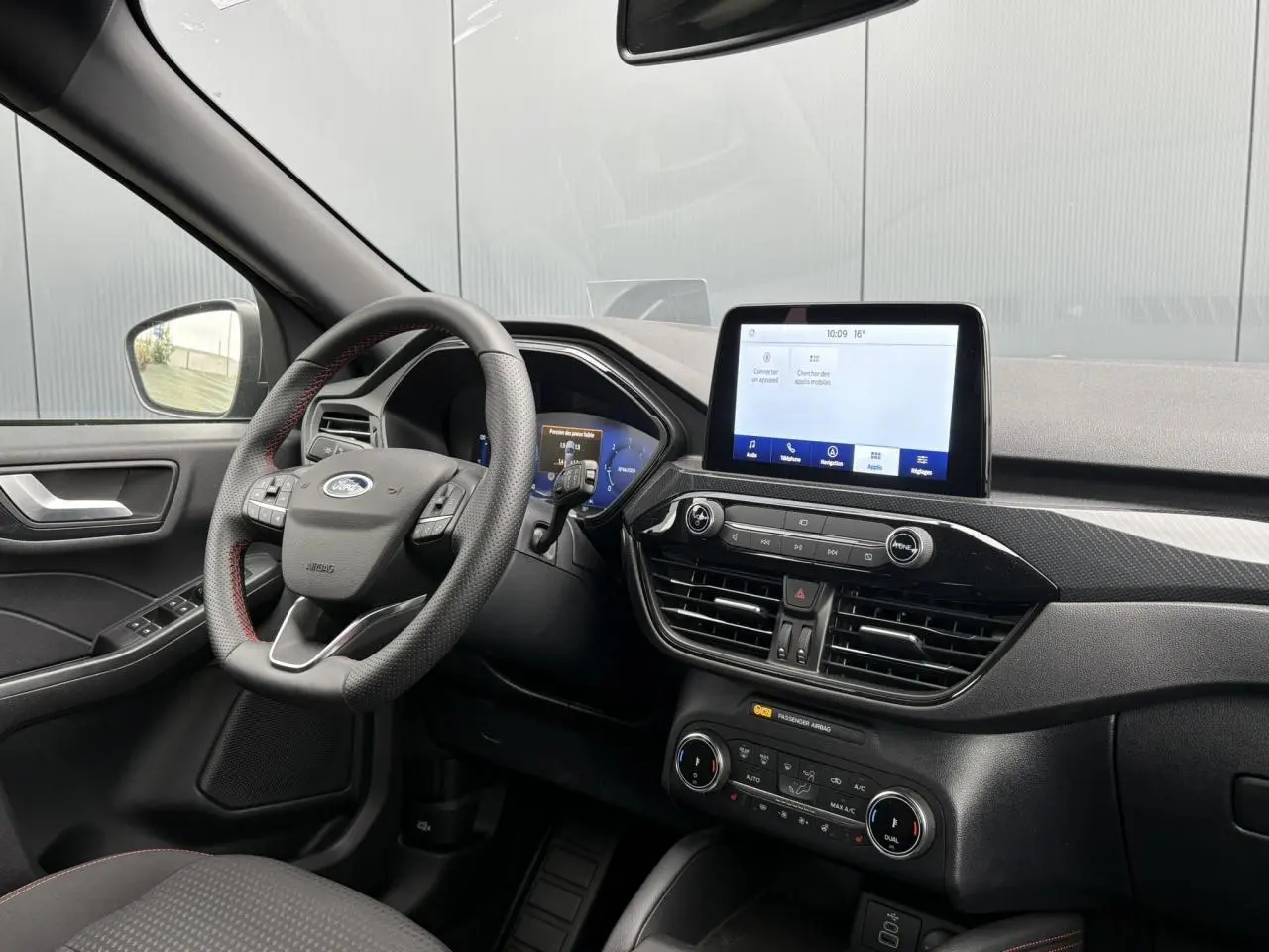 Vue intérieure côté conducteur du Ford Kuga gris graphite 2023, volant ST-Line à surpiqûres rouges et écran tactile central.