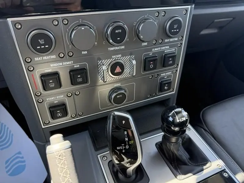 Gros plan intérieur sur la console centrale beige de l'INEOS Grenadier 2024 avec commandes clim et levier de boîte automatique.