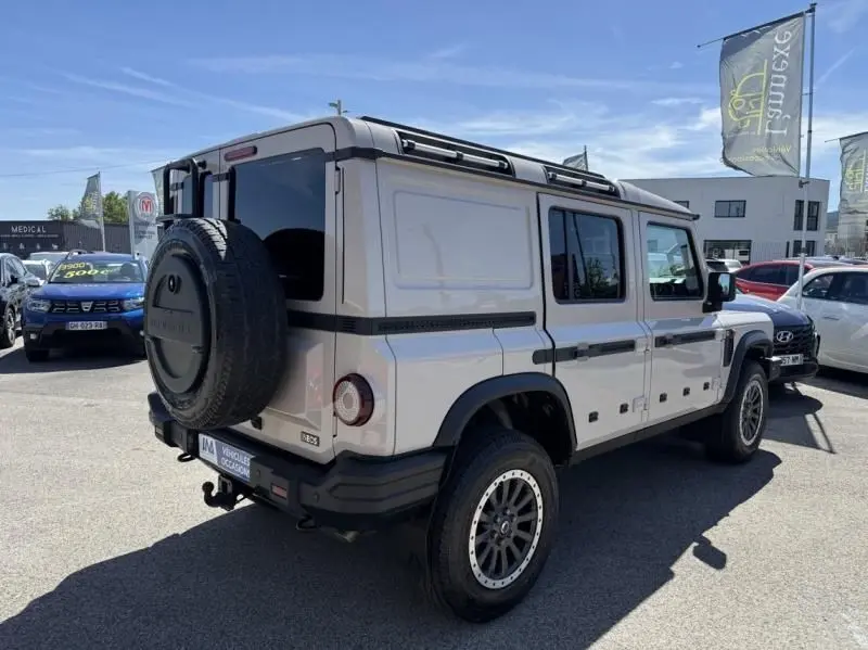 Vue 3/4 arrière droite de l'INEOS Grenadier beige 2024 avec roue de secours et châssis cab visible en extérieur.