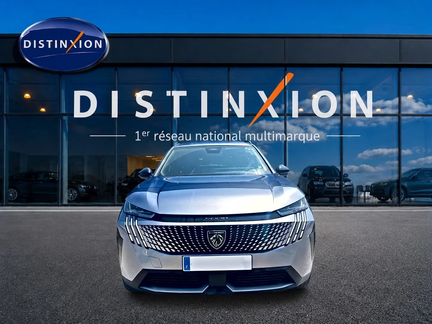 Vue frontale du Peugeot 5008 Hybrid 145 allure e-dcs6 gris artense devant une vitrine Distinxion.