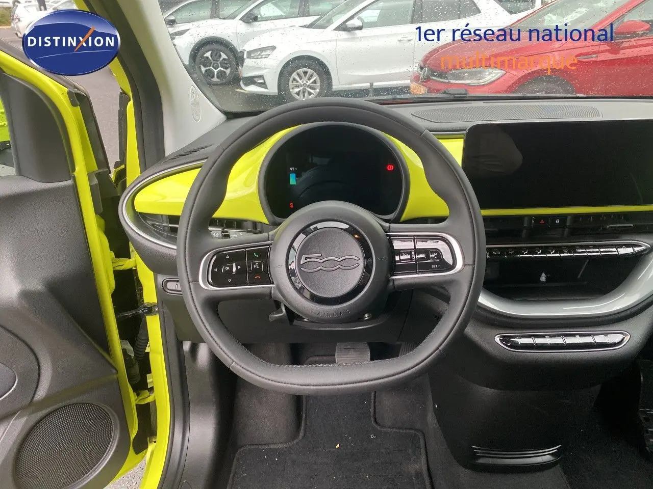 Vue intérieure avant de la Fiat 500 électrique 2024 jaune acid, avec volant multifonction et tableau de bord moderne.
