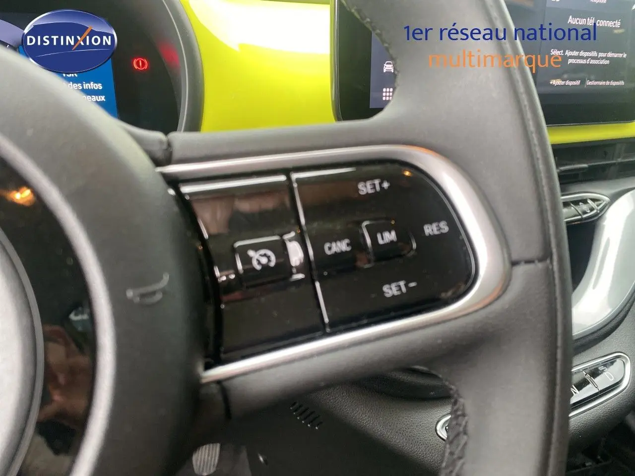 Gros plan sur le volant côté gauche d'une Fiat 500 électrique jaune acid, avec commandes de régulateur de vitesse visibles.