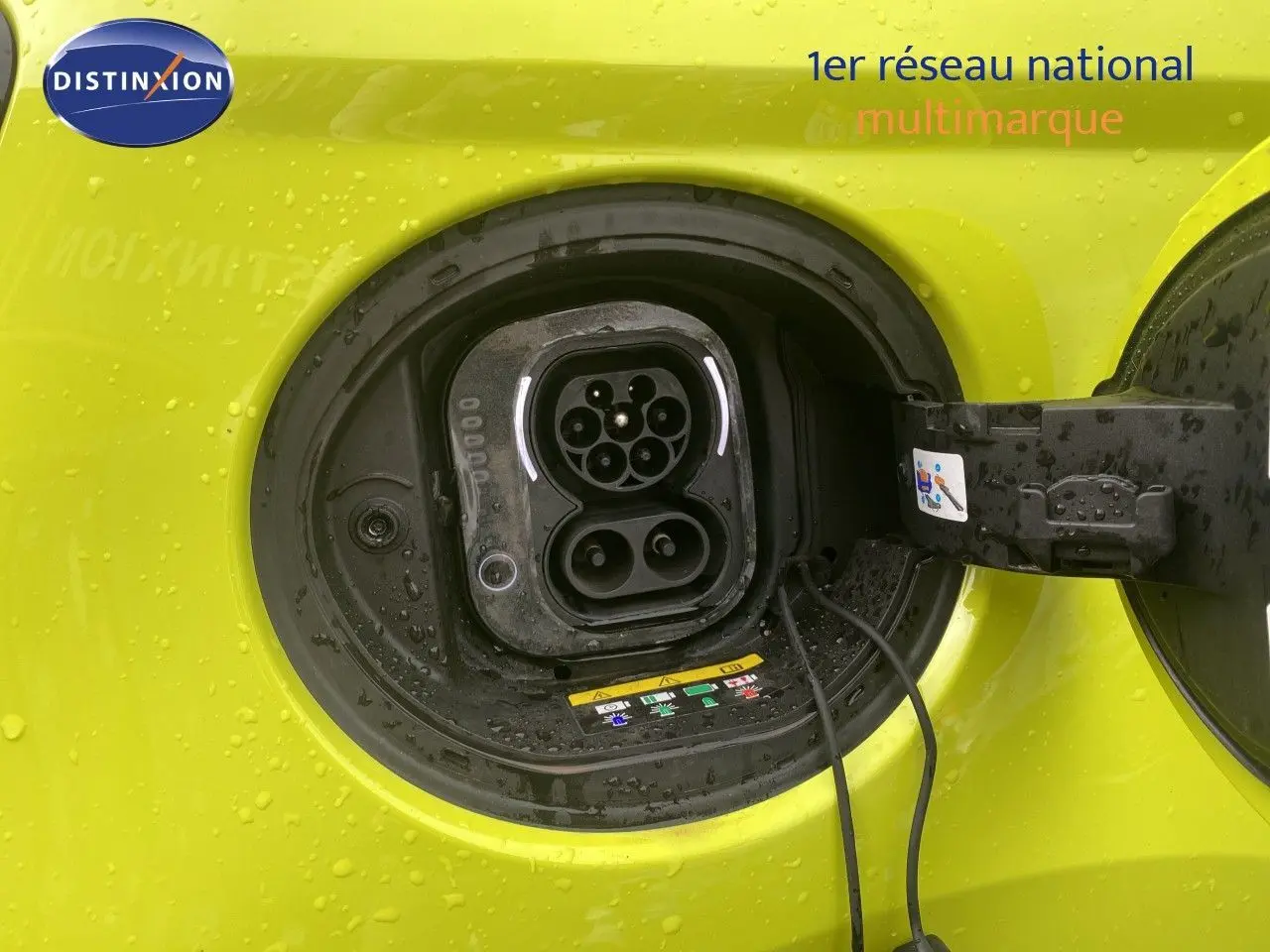 Prise de recharge électrique ouverte sur la côté gauche d'une FIAT 500 jaune acid 2024, avec gouttes d'eau visibles.