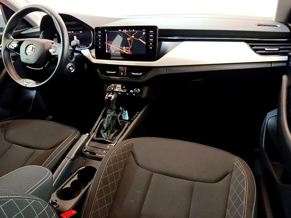Intérieur du Skoda Kamiq 2022 vu côté conducteur, tableau de bord noir avec écran tactile et sièges tissu gris foncé.