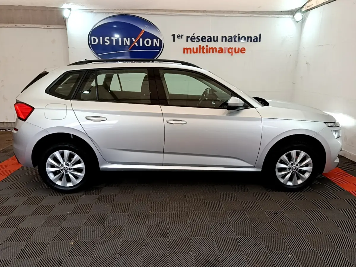 Profil latéral droit d'un Skoda Kamiq gris clair 2022 garé en intérieur avec rails de toit noirs visibles.