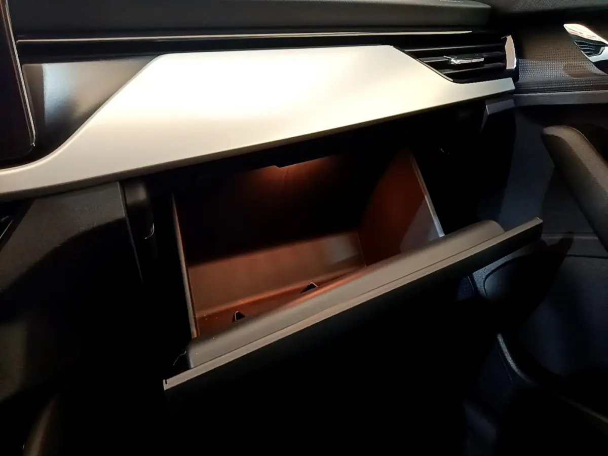 Intérieur du Skoda Kamiq 2022, vue sur la boîte à gants ouverte avec éclairage intérieur et tableau de bord gris clair.