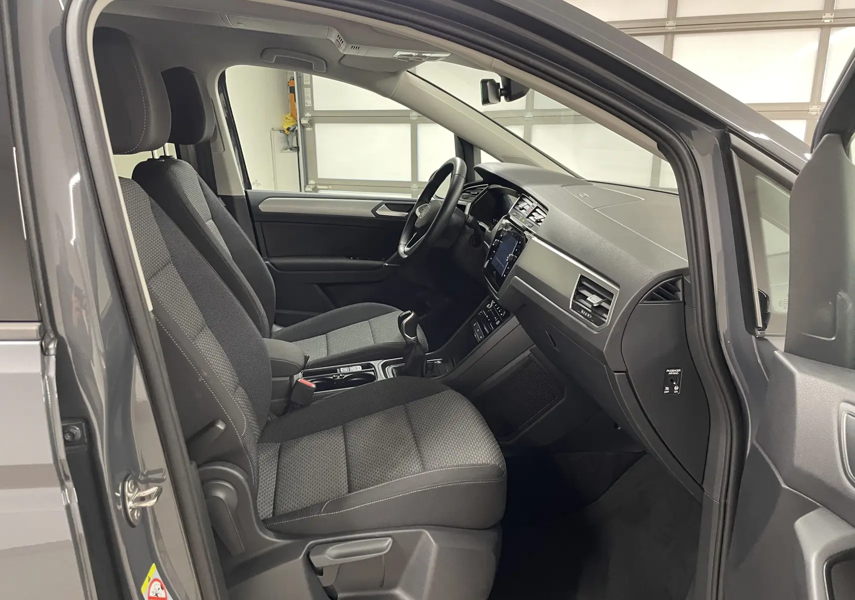 Vue intérieure côté conducteur du Volkswagen Touran gris Dauphin 2024, montrant sièges et tableau de bord modernes.