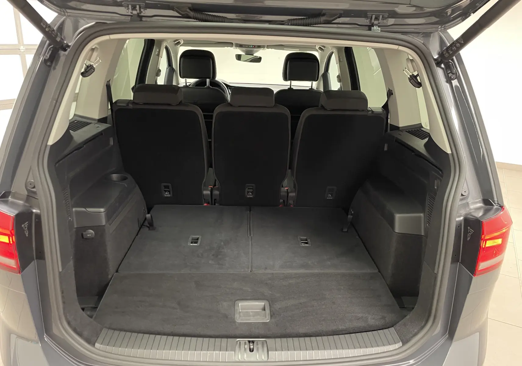 Vue arrière du coffre ouvert d'un Volkswagen Touran gris Dauphin 2024, montrant les sièges arrière relevés et l'espace de chargement.