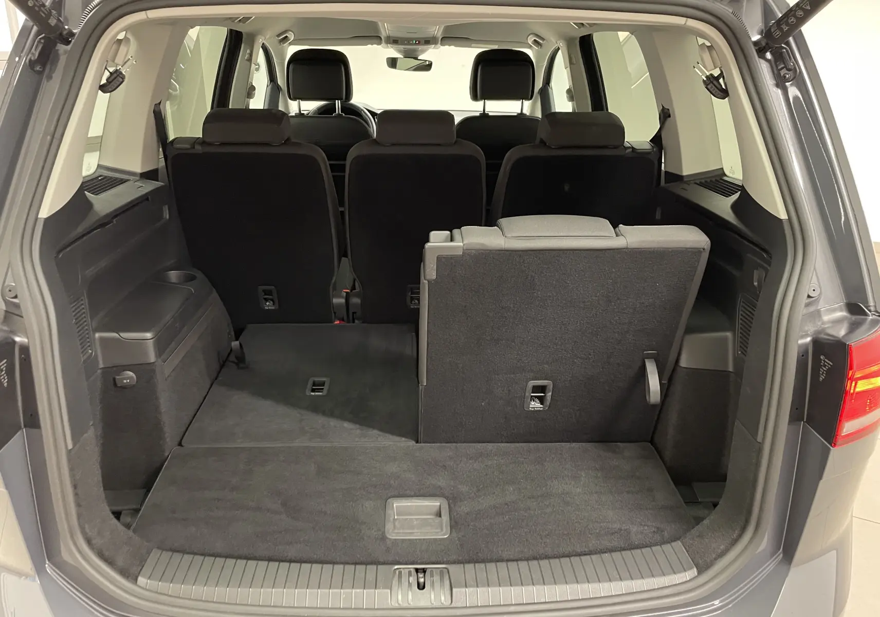 Vue arrière du coffre ouvert du Volkswagen Touran gris dauphin 2024, montrant la banquette arrière partiellement rabattue.