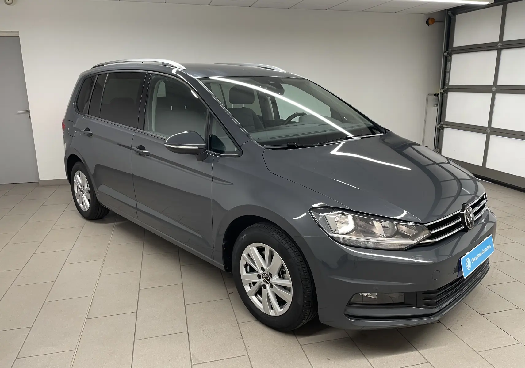 Volkswagen Touran gris dauphin en 3/4 avant droit, montrant ses lignes épurées et ses jantes alliage.