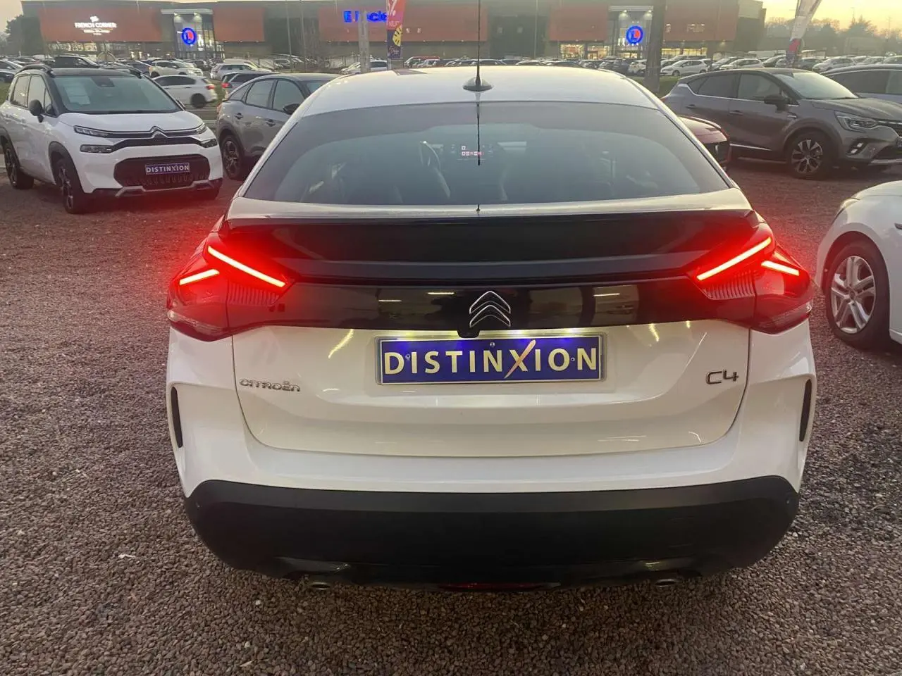 Vue arrière d'une Citroën C4 blanche 2021 avec feux arrière allumés et plaque Distinxion visible.