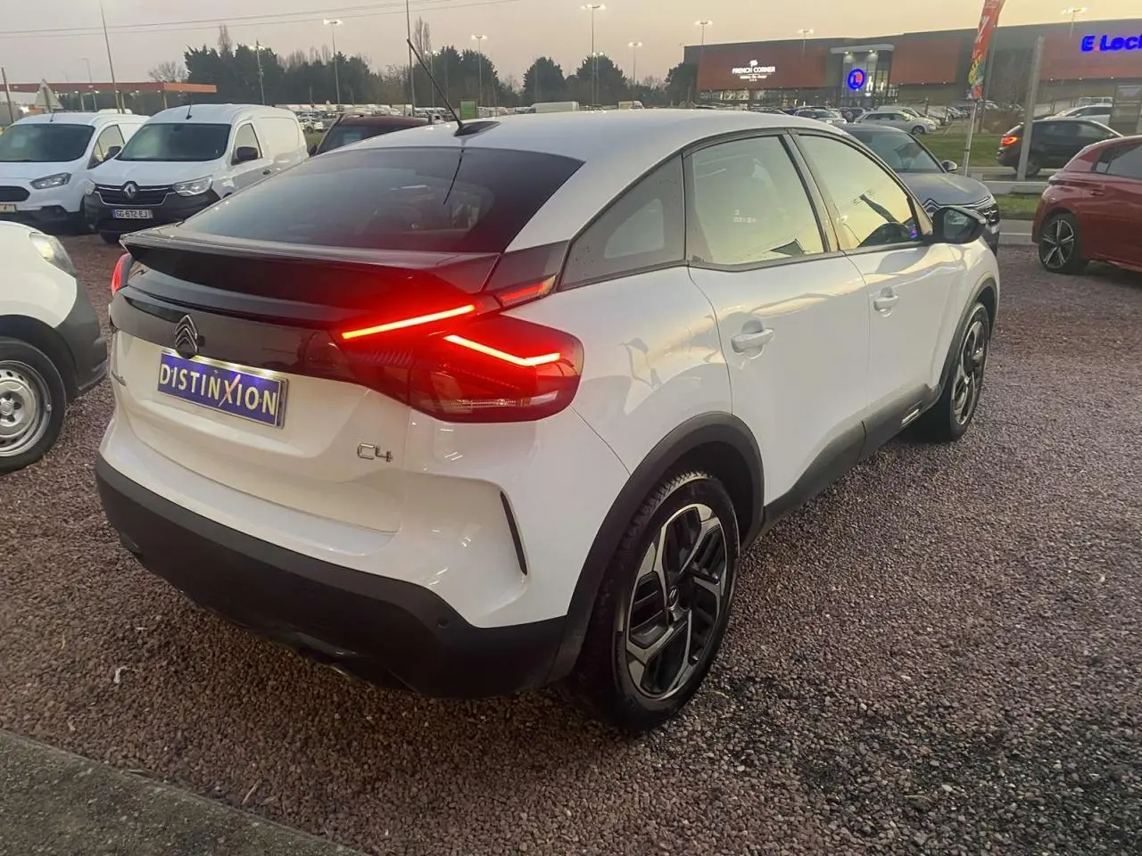 Vue 3/4 arrière droite d'une Citroën C4 blanche 2021 avec feux arrière allumés et toit noir contrastant.